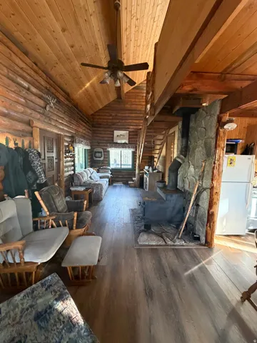 Living area with a wood stove, hardwood / wood-style floors, a vaulted wooden ceiling, a ceiling fan, and log walls