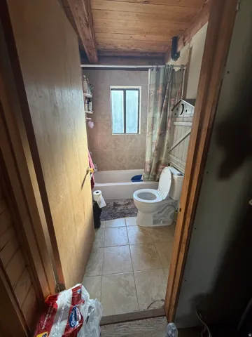 Full bathroom with light tile patterned floors, wooden ceiling, and shower / bath combo with shower curtain