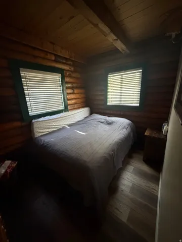 Bedroom with rustic walls, a wooden ceiling with exposed beams, and dark wood finished floors