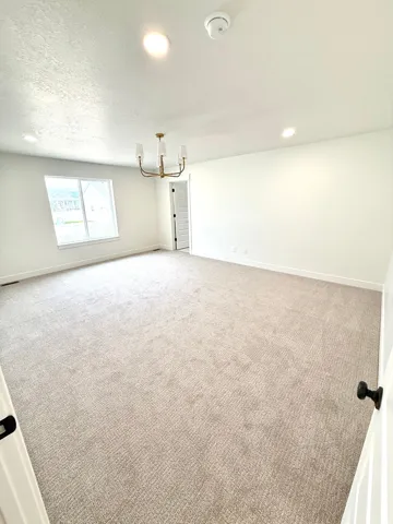 Spacious room featuring neutral carpeting, white walls, and a contemporary brass chandelier