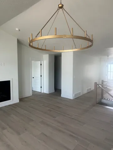 Spacious interior featuring a large gold-finish chandelier, light wood-finish flooring, a contemporary fireplace, white baseboards, and a modern stair railing