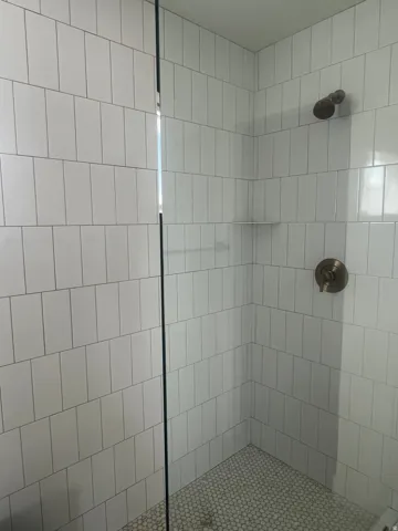 Shower enclosure featuring white vertical subway tile, glass shower panel, bronze shower fixtures, and a white penny tile shower pan