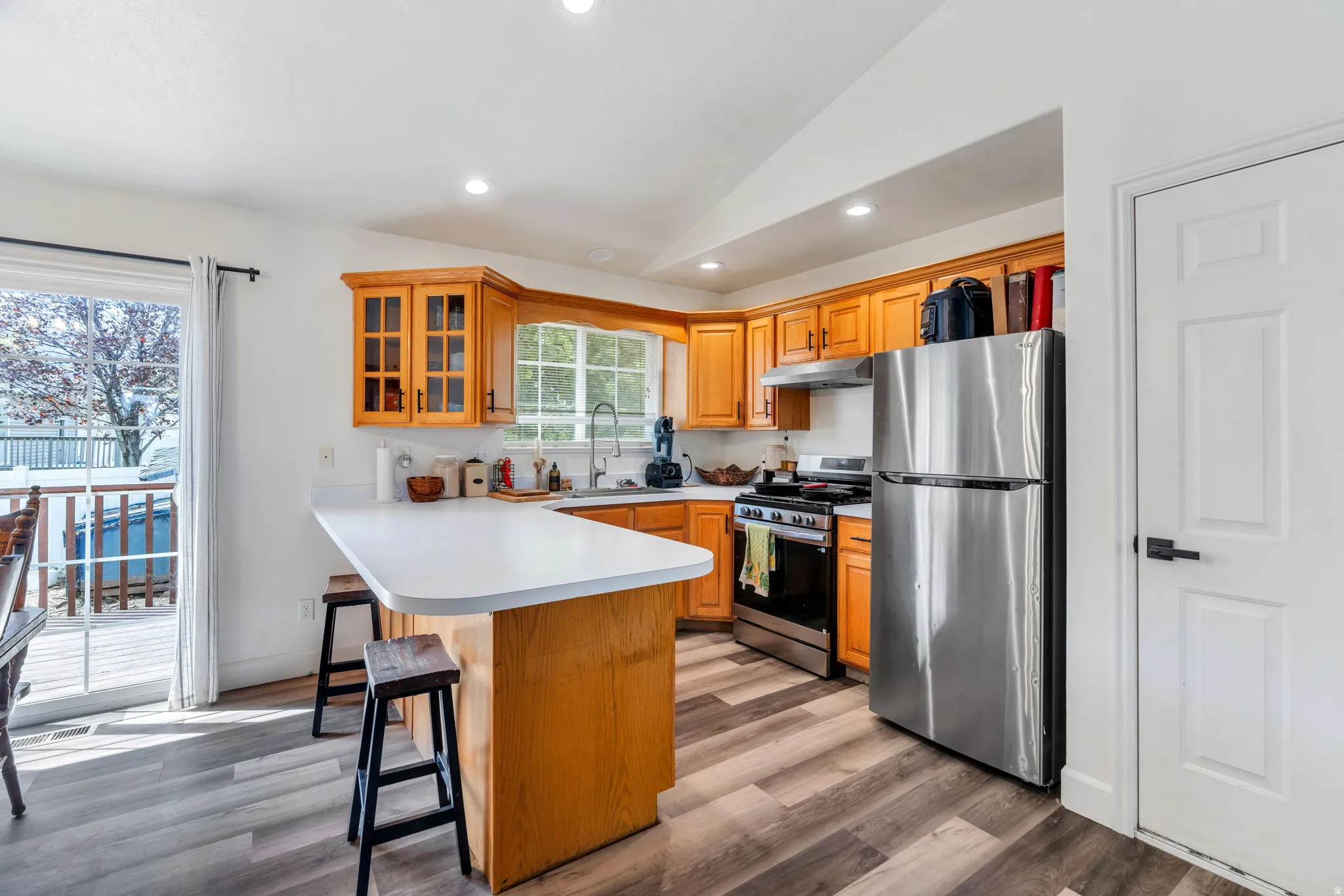 Kitchen featuring newer appliances, a breakfast bar area, a peninsula, light countertops, and glass insert cabinets