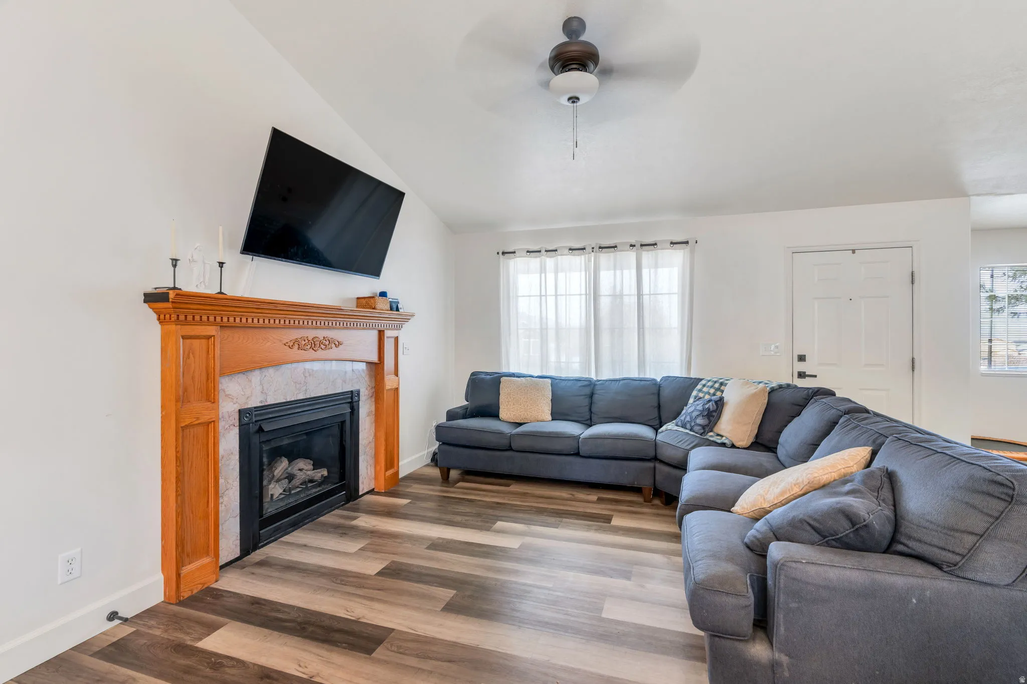 Living area with LVP wood finished floors, vaulted ceiling, ceiling fan, and a gas fireplace