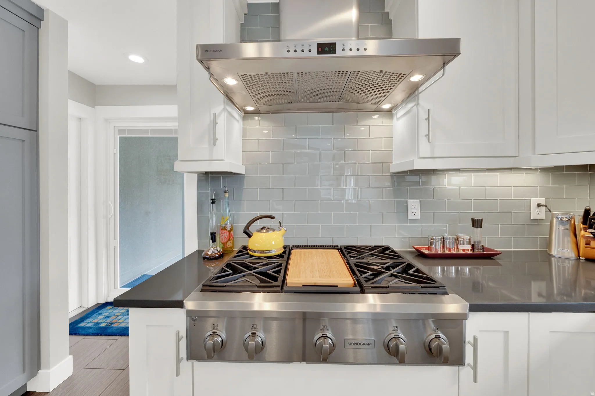 Kitchen featuring extractor fan, stainless steel gas cooktop, white cabinetry, recessed lighting, and dark quartz countertops