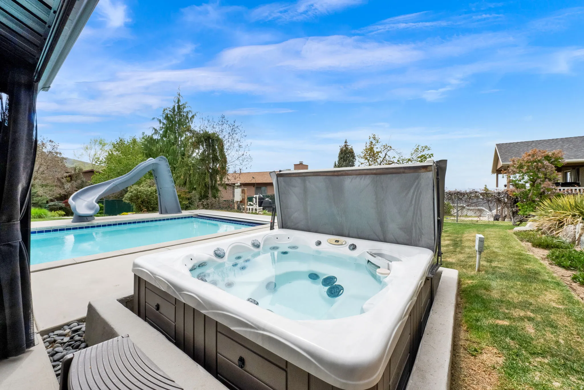 View of pool featuring a water slide, patio surround, and an outdoor hot tub
