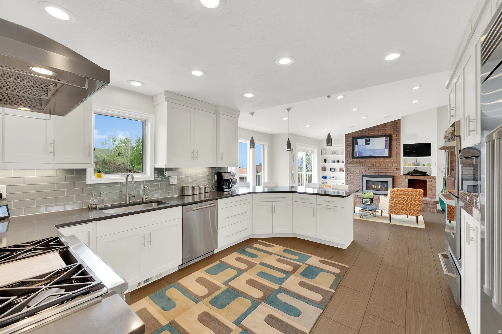 Kitchen featuring a fireplace, decorative light fixtures, white cabinets, stainless steel appliances, and vaulted ceiling