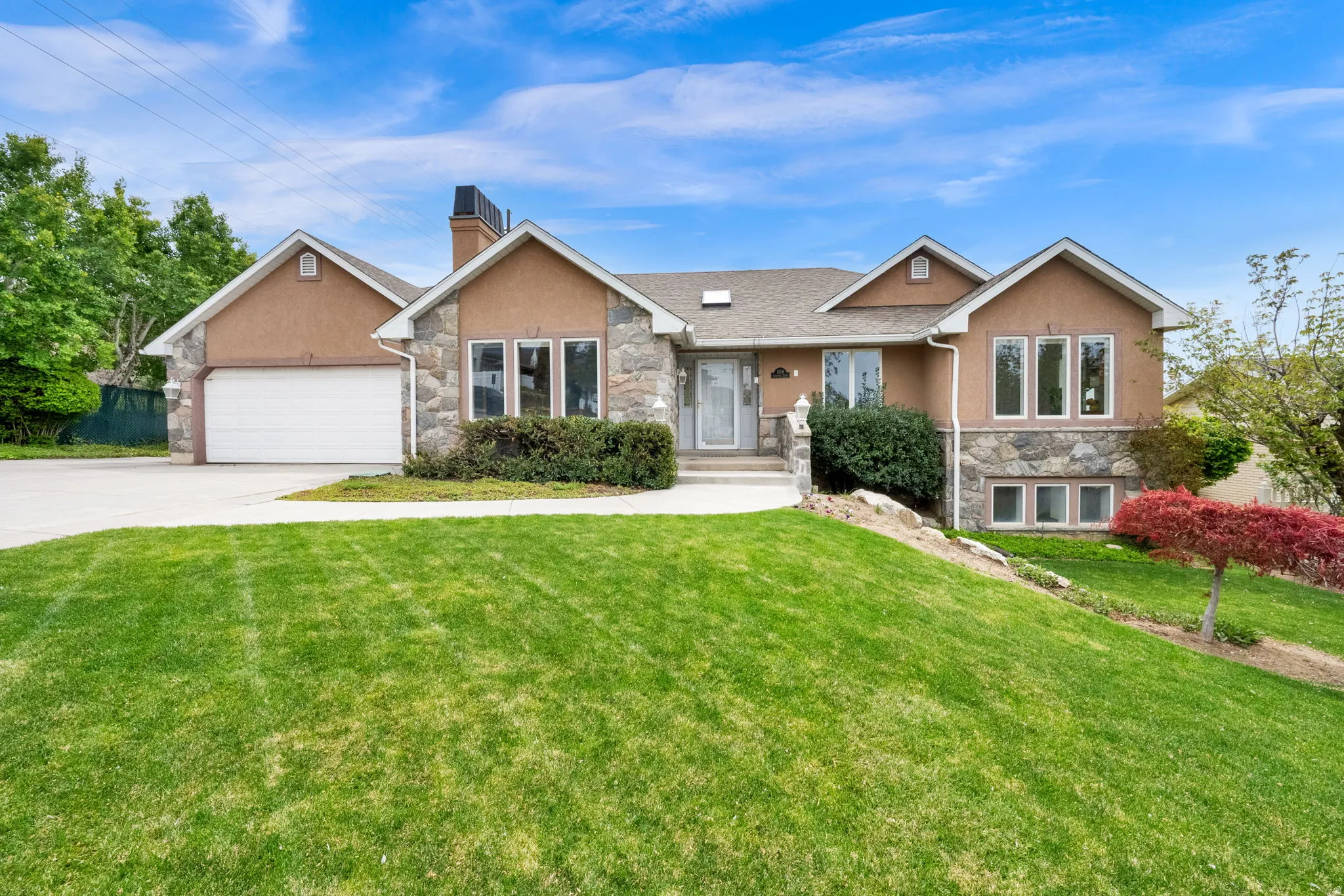 View of front of property featuring stone siding, an attached garage, driveway, and stucco siding