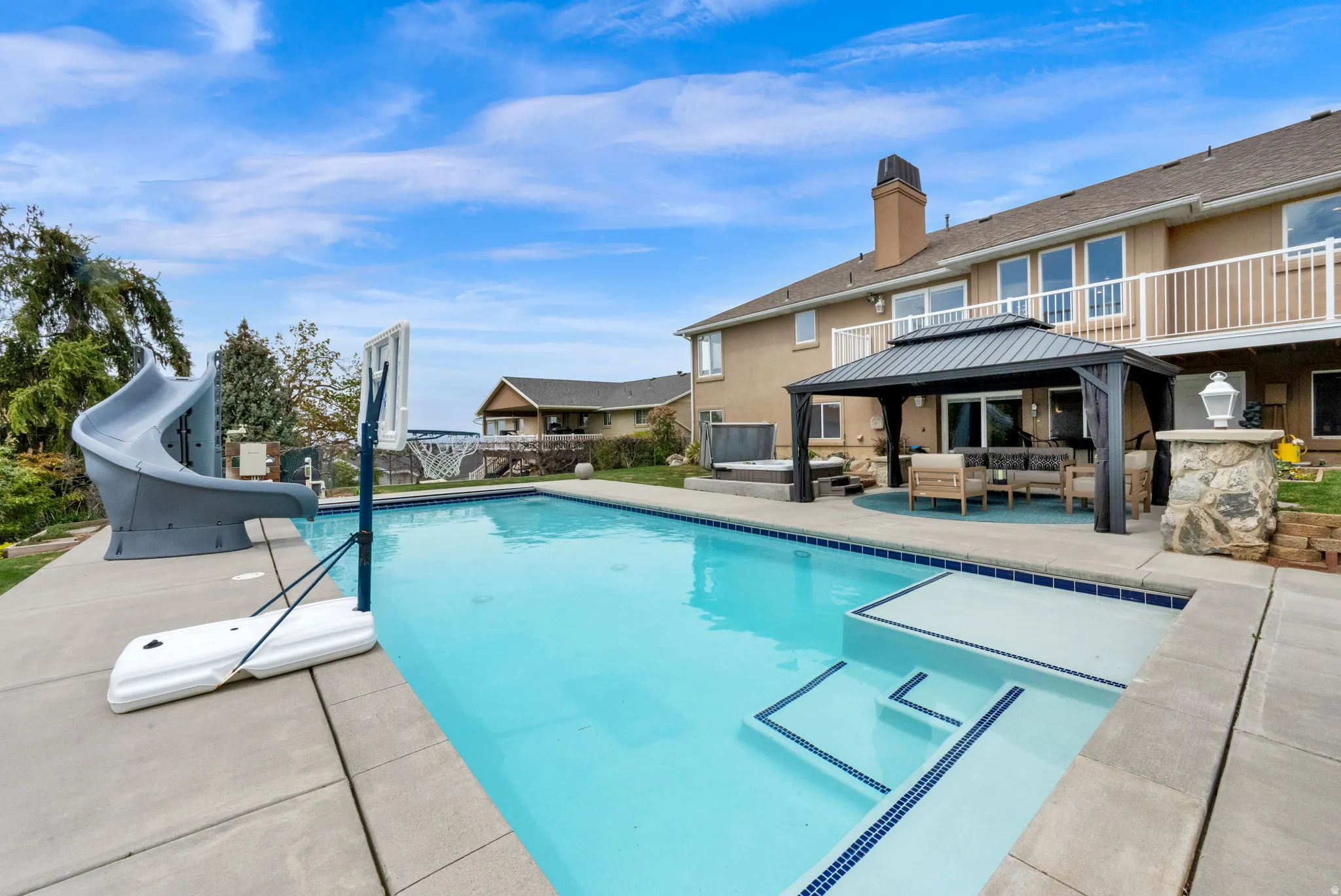 View of pool featuring patio surround, a water slide, outdoor lounge area, and a gazebo