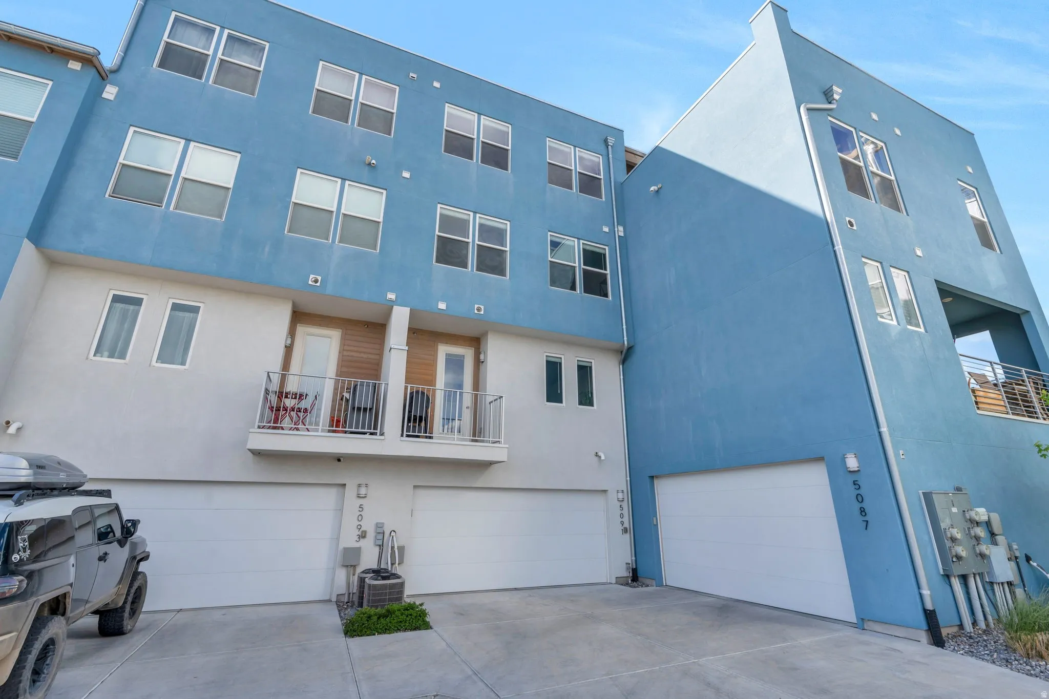 Back of house with a balcony, an attached garage, stucco siding, and driveway