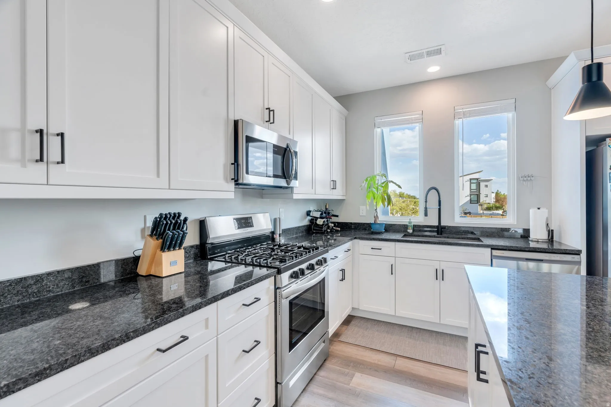 Kitchen featuring stainless steel appliances, white cabinetry, dark stone countertops, light wood-style flooring, and pendant lighting