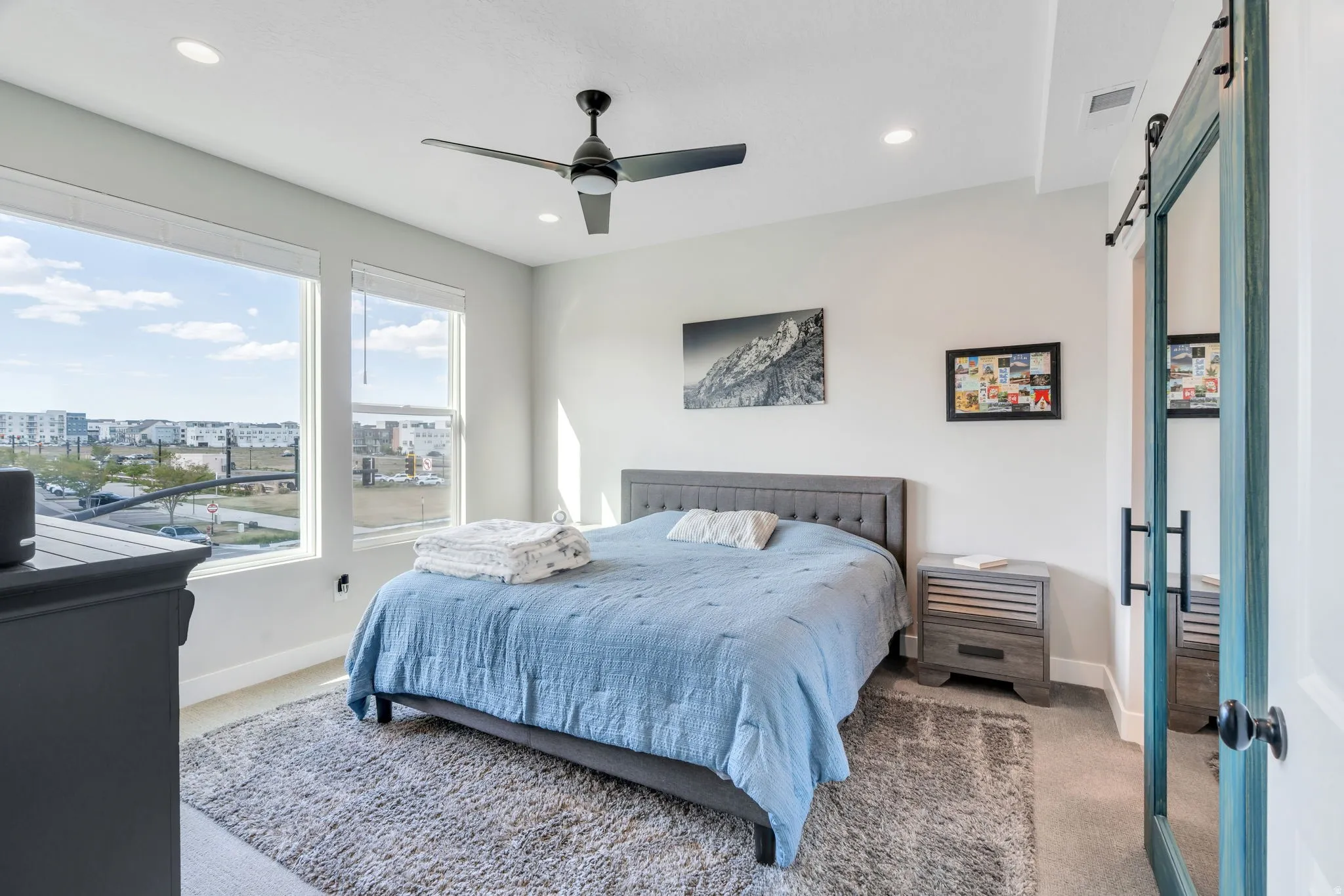 Carpeted bedroom with a barn door, a ceiling fan, recessed lighting, and a city view