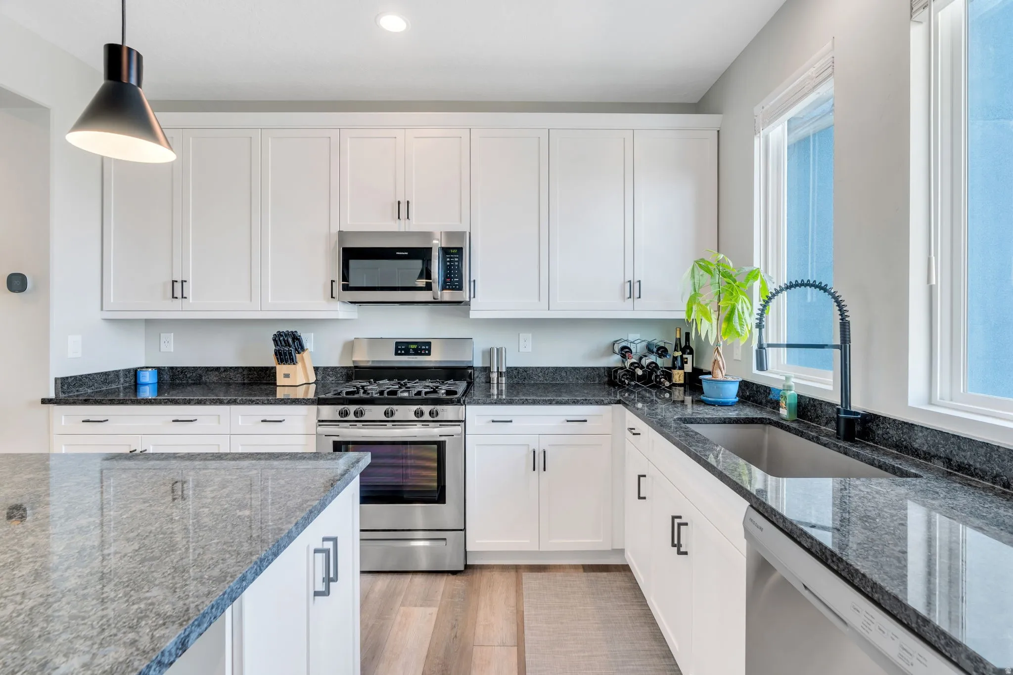 Kitchen with stainless steel appliances, dark stone countertops, white cabinetry, and hanging light fixtures