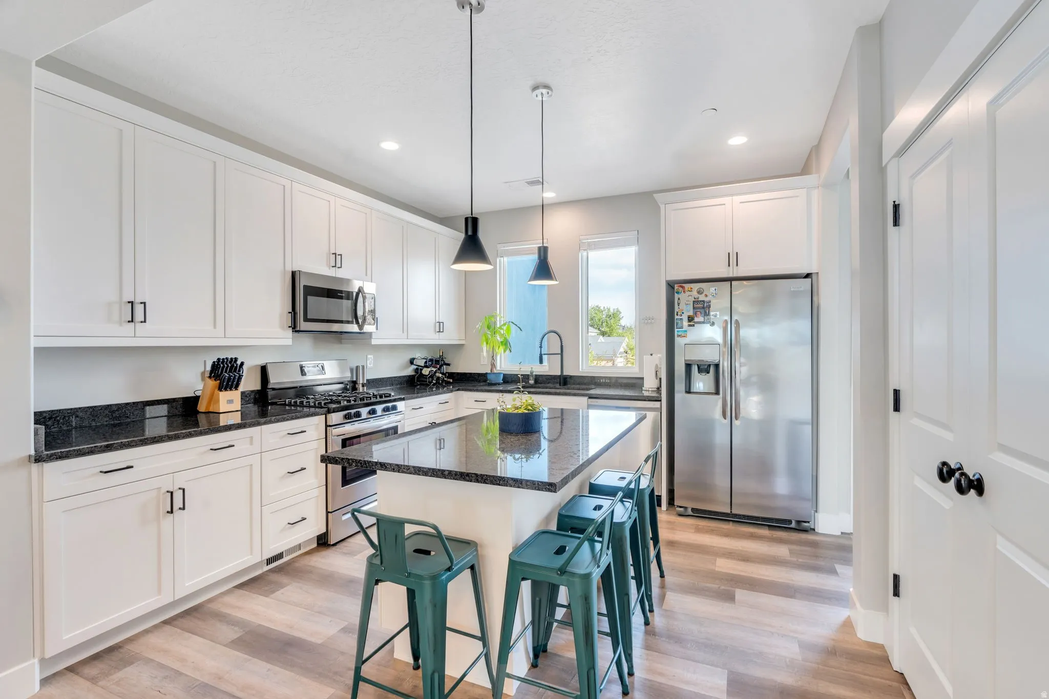 Kitchen featuring dark stone counters, stainless steel appliances, white cabinets, and light wood-style floors