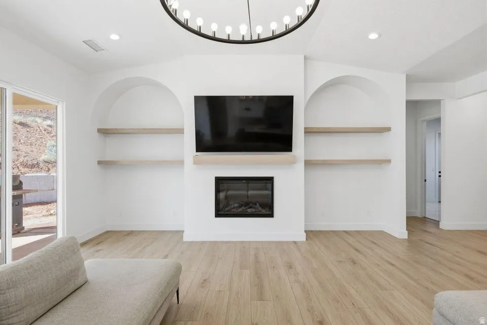 Living area featuring built in shelves, light wood-type flooring, a glass covered fireplace, and recessed lighting