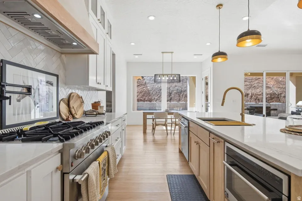 Kitchen with two tone cabinetry, stainless steel appliances, light stone counters, decorative backsplash, and light wood-style flooring