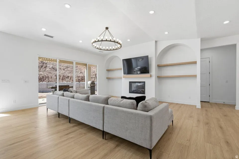 Living area with built in shelves, a glass covered fireplace, light wood-type flooring, and a chandelier