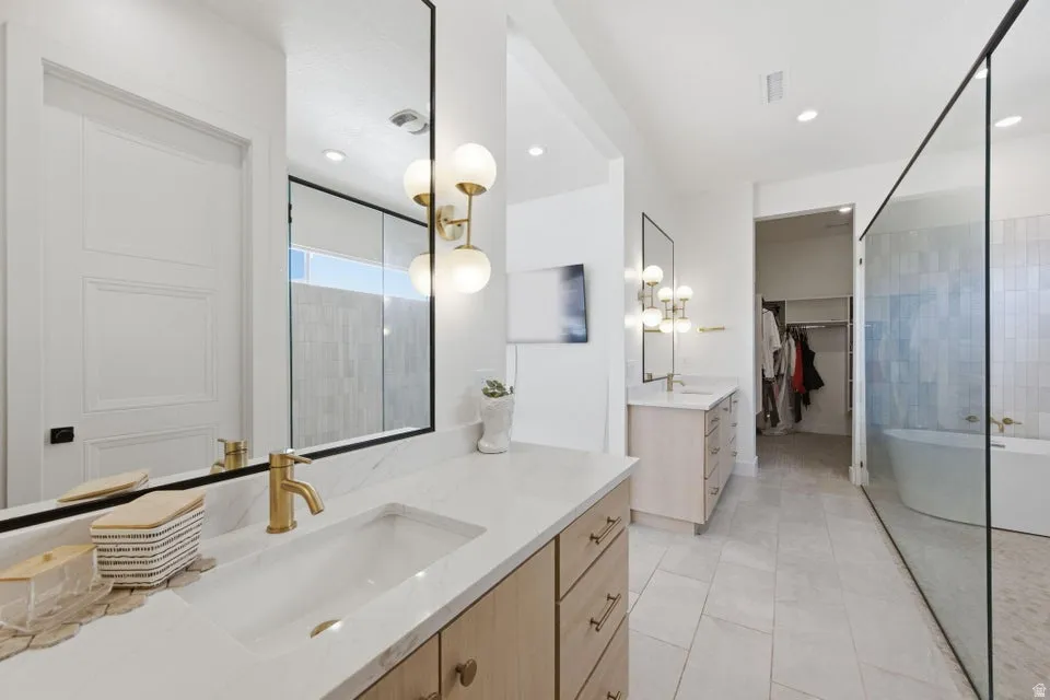Full bath featuring a walk in closet, a freestanding tub, two vanities, recessed lighting, and light tile patterned floors