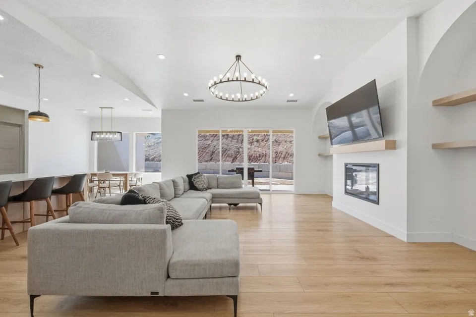 Living room featuring a glass covered fireplace, hanging lights, and light wood-style floors