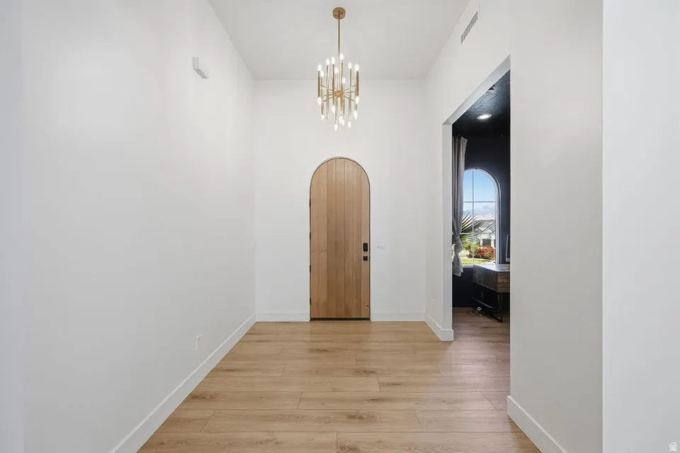 Corridor with arched walkways, light wood-style flooring, and suspended lighting