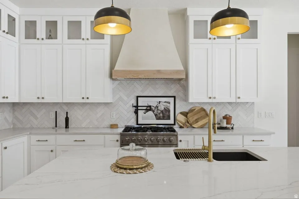 Kitchen with glass fronted cabinets, white cabinets, and light stone counters