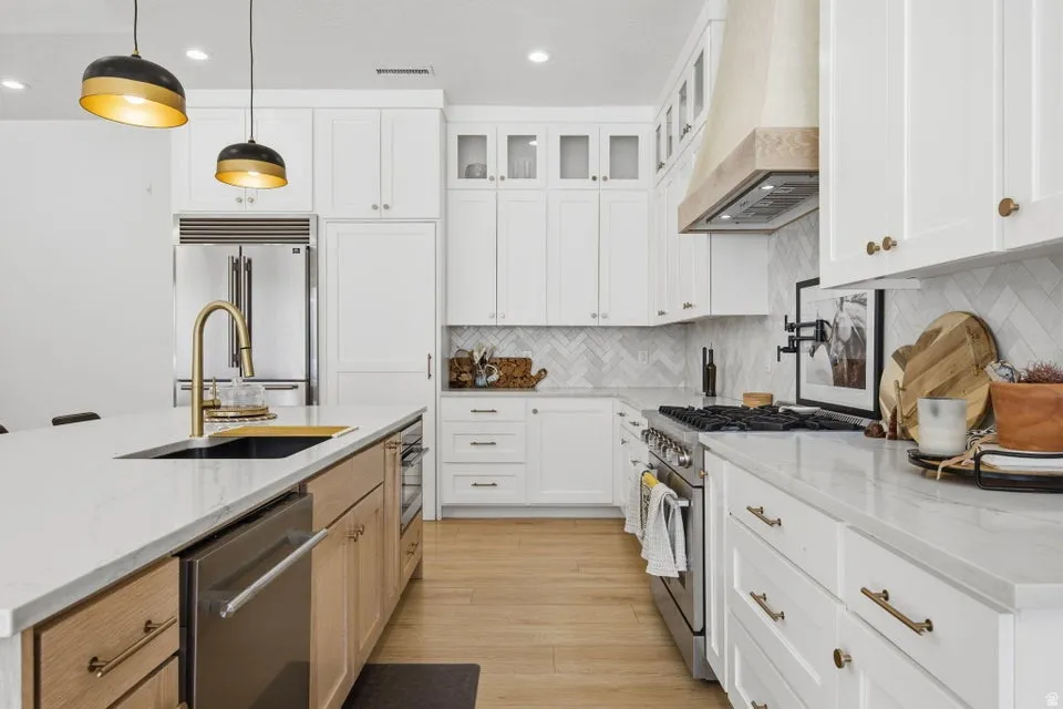 Two tone kitchen with light stone counters, premium appliances, two tone cabinets, pendant lighting, and light wood-style flooring