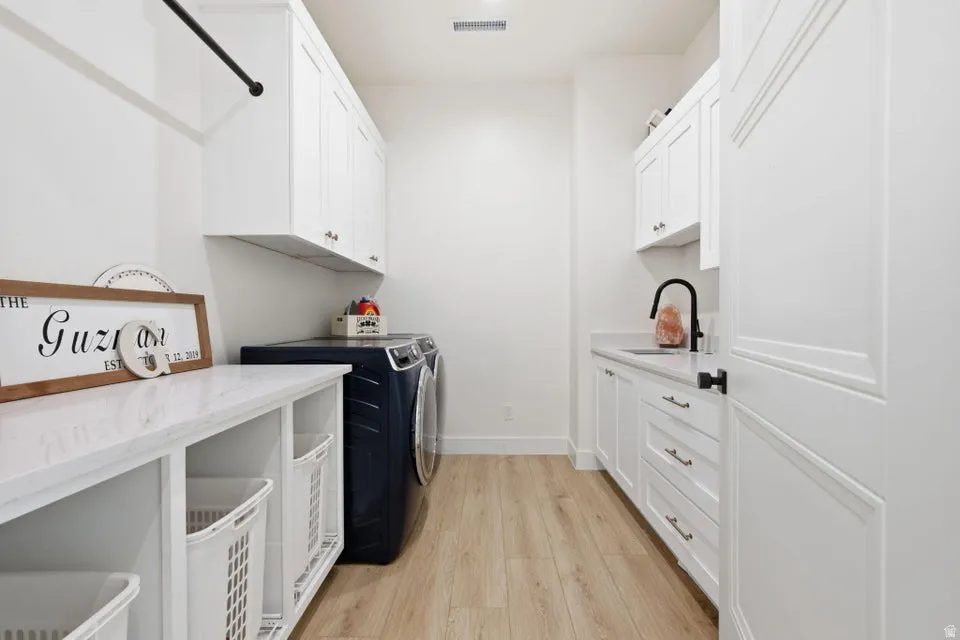 Laundry room with light wood finished floors, washer and clothes dryer, and cabinet space