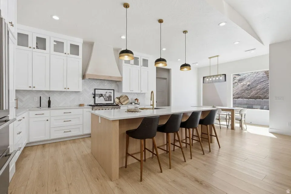 Kitchen with pendant lighting, a center island with sink, light stone counters, a kitchen bar, and light wood finished floors
