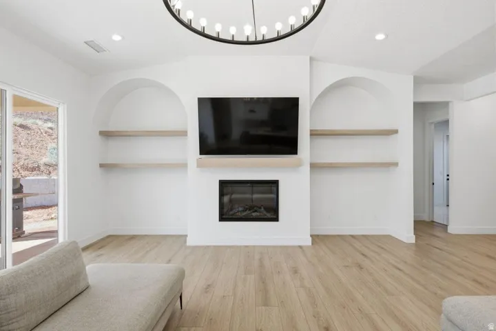 Living area featuring built in shelves, light wood-type flooring, a glass covered fireplace, and recessed lighting