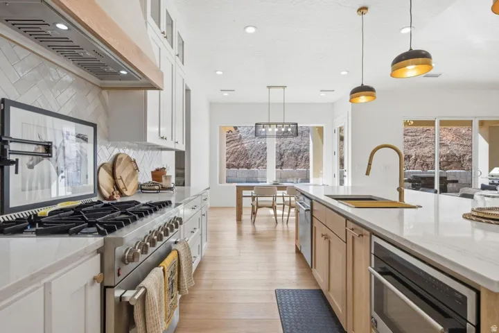 Kitchen with two tone cabinetry, stainless steel appliances, light stone counters, decorative backsplash, and light wood-style flooring