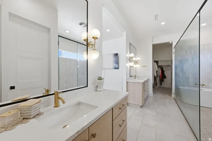 Full bath featuring a walk in closet, a freestanding tub, two vanities, recessed lighting, and light tile patterned floors