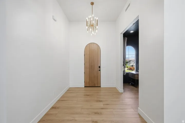 Corridor with arched walkways, light wood-style flooring, and suspended lighting