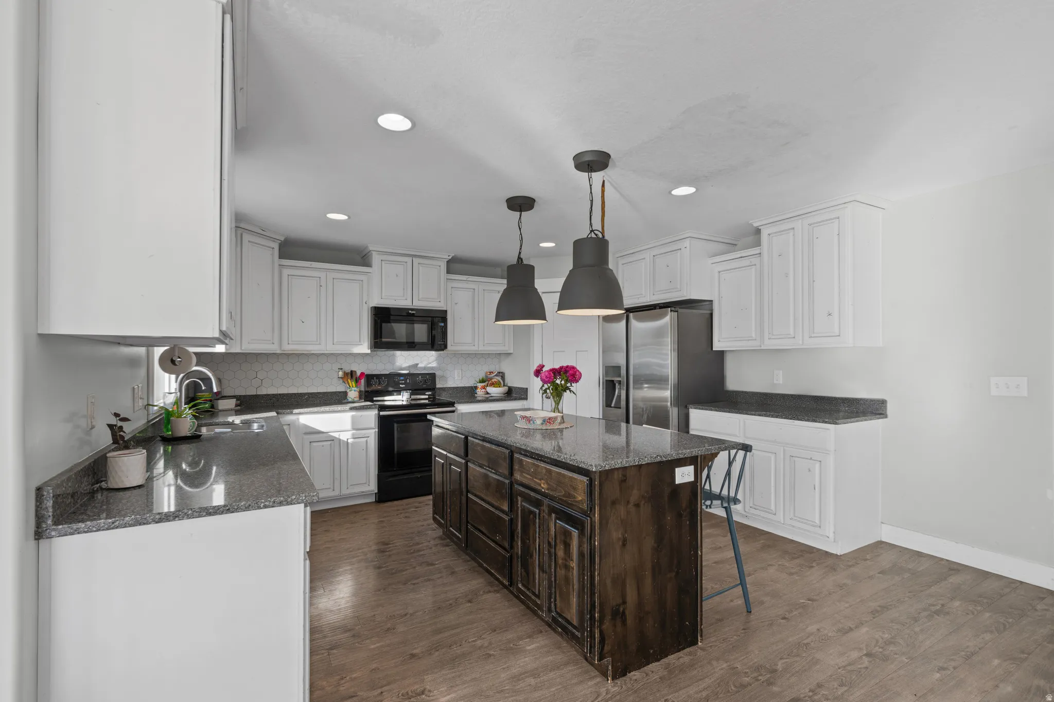Two tone kitchen with dual tone cabinetry, dark stone countertops, black appliances, a kitchen breakfast bar, and a center island
