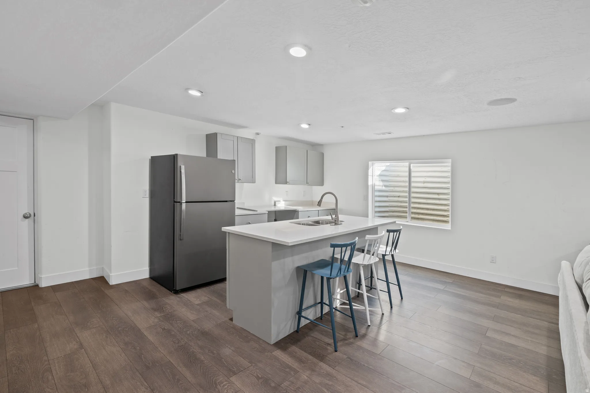 Kitchen with freestanding refrigerator, gray cabinets, an island with sink, dark wood-type flooring, and a breakfast bar