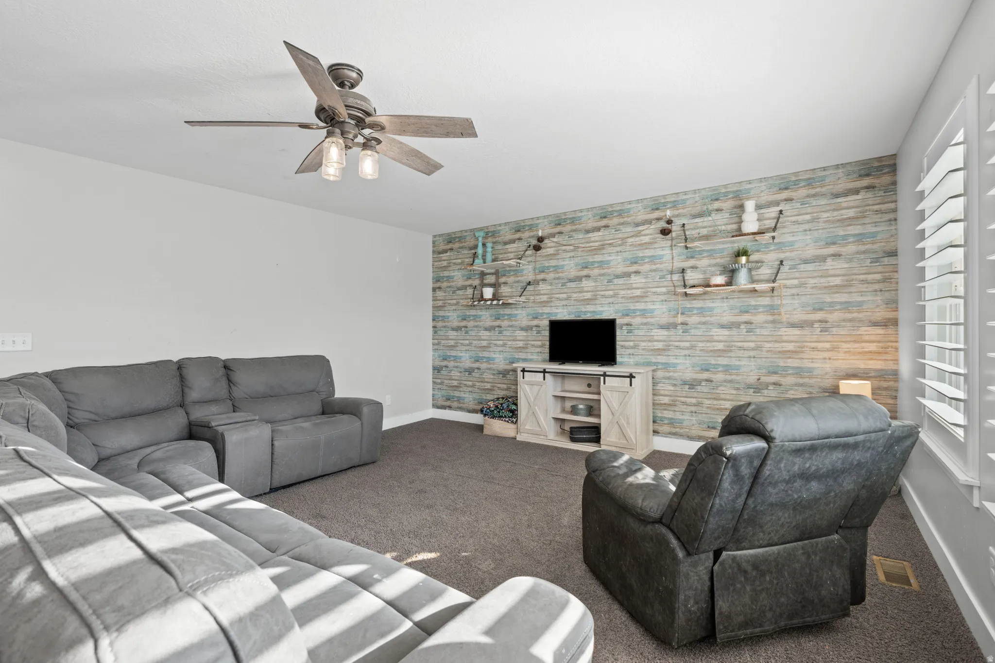 Living room featuring an accent wall, carpet, and ceiling fan