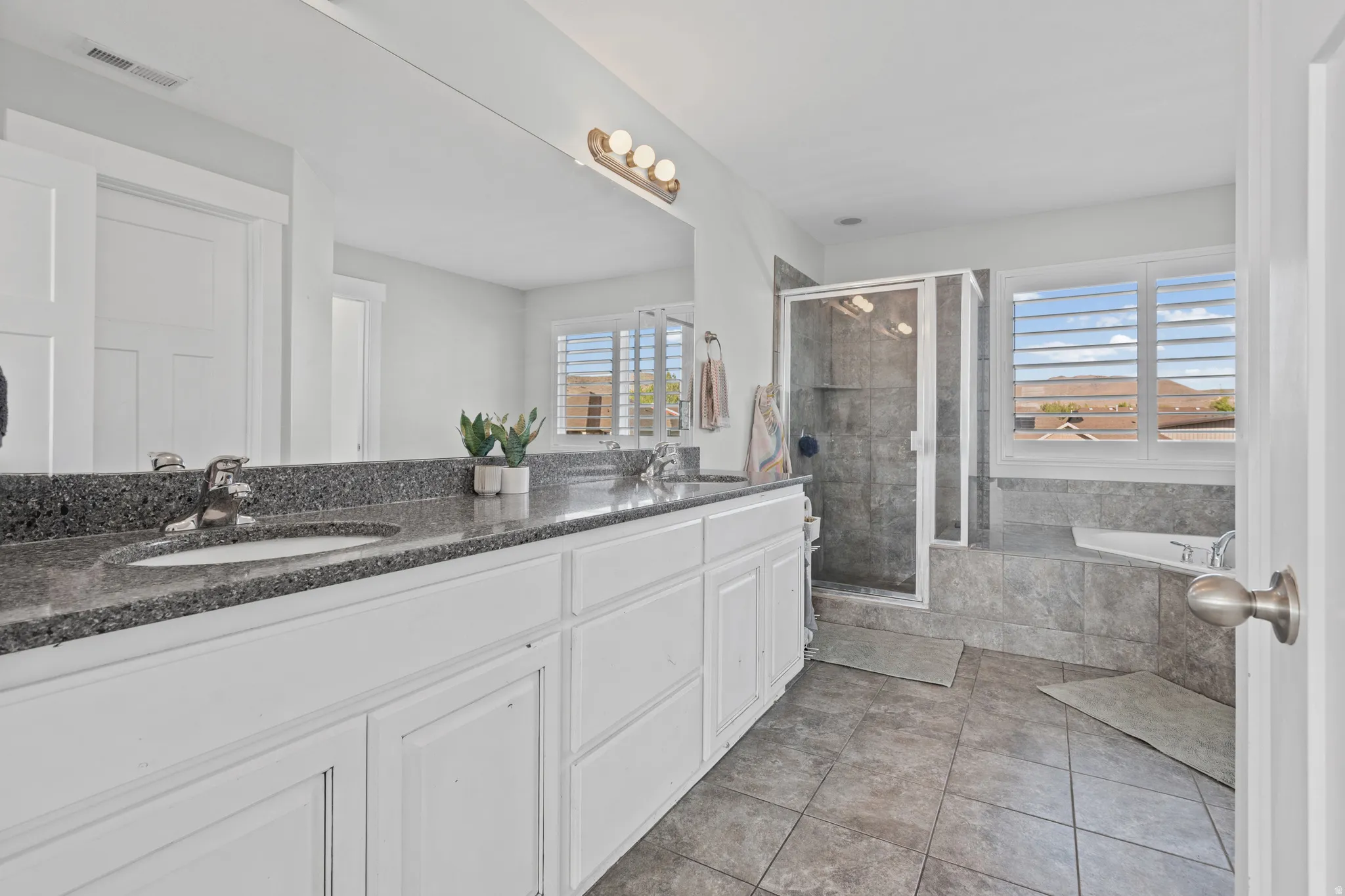 Bathroom featuring double vanity, a garden tub, a stall shower, and light tile patterned floors