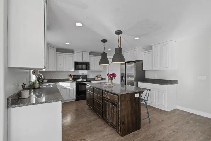 Two tone kitchen with dual tone cabinetry, dark stone countertops, black appliances, a kitchen breakfast bar, and a center island