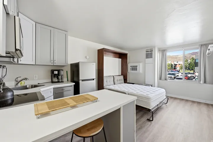 Kitchen with light countertops, a breakfast bar area, freestanding refrigerator, gray cabinetry, and light wood finished floors