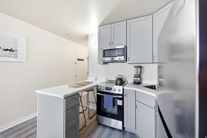 Kitchen featuring stainless steel appliances, a peninsula, gray cabinetry, a kitchen bar, and dark wood-style flooring