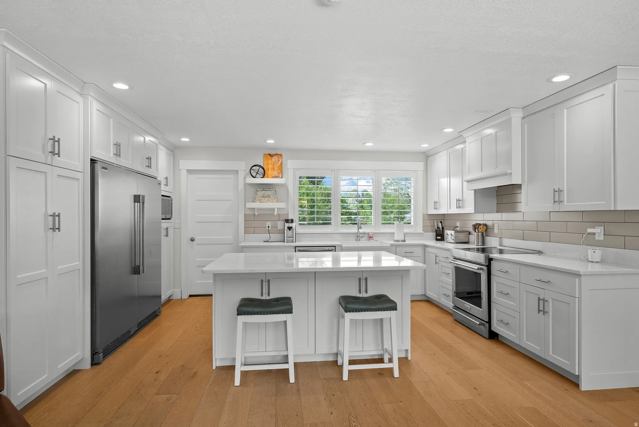 Kitchen with open shelves, white cabinets, stainless steel appliances, a breakfast bar area, and recessed lighting