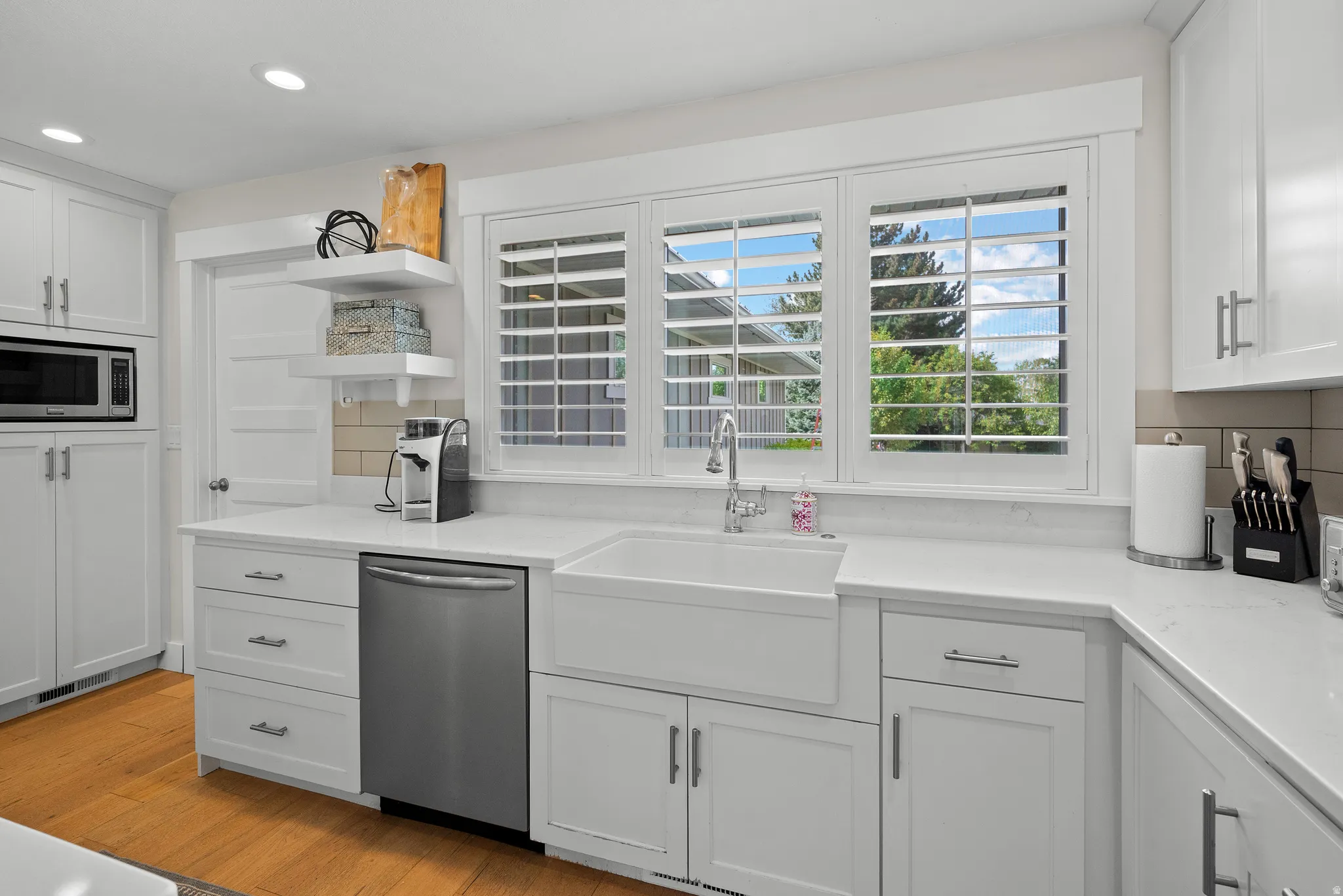 Kitchen with white cabinetry, stainless steel appliances, light wood-style flooring, light stone counters, and open shelves