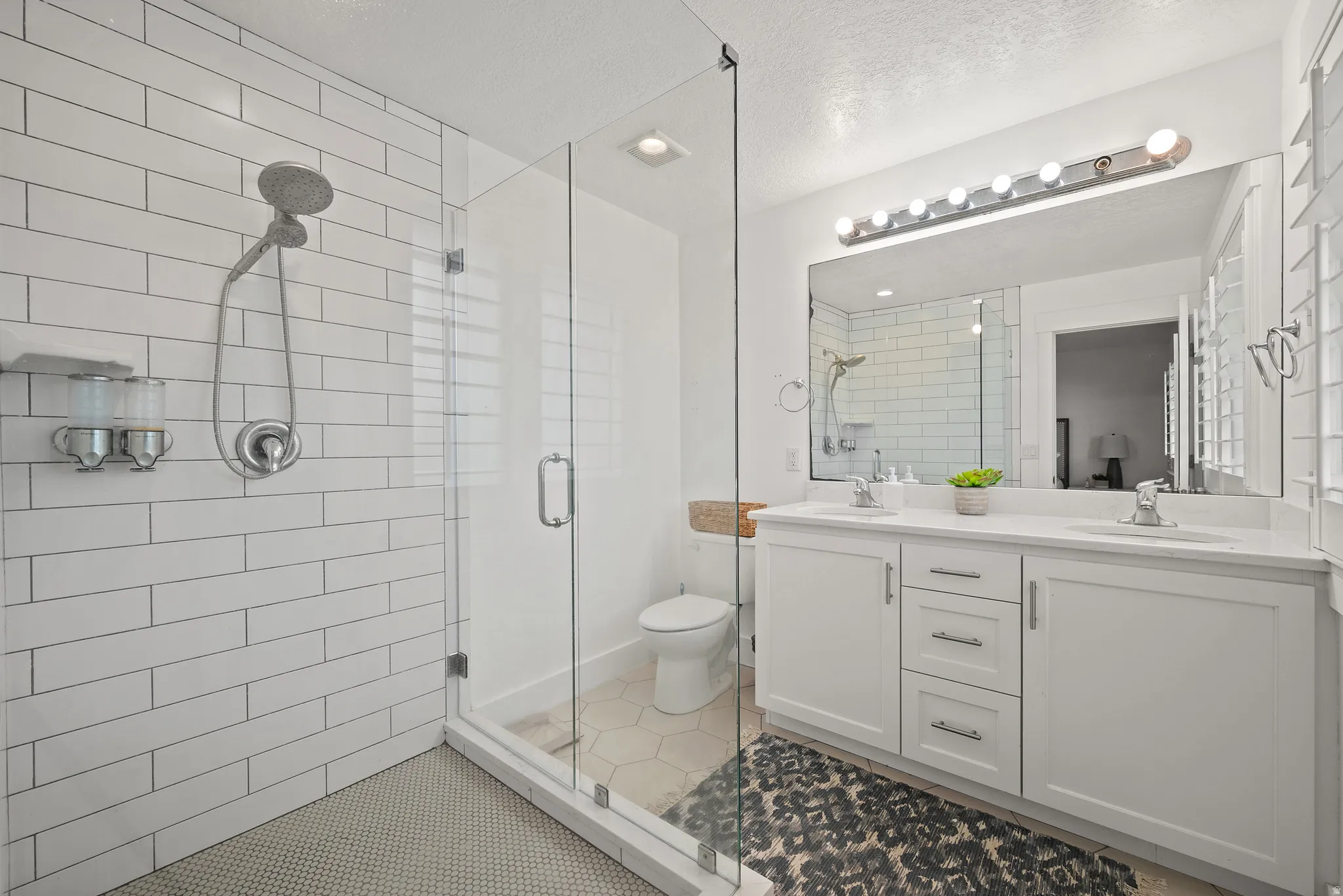 Bathroom featuring double vanity, light tile patterned floors, a stall shower, and a textured ceiling