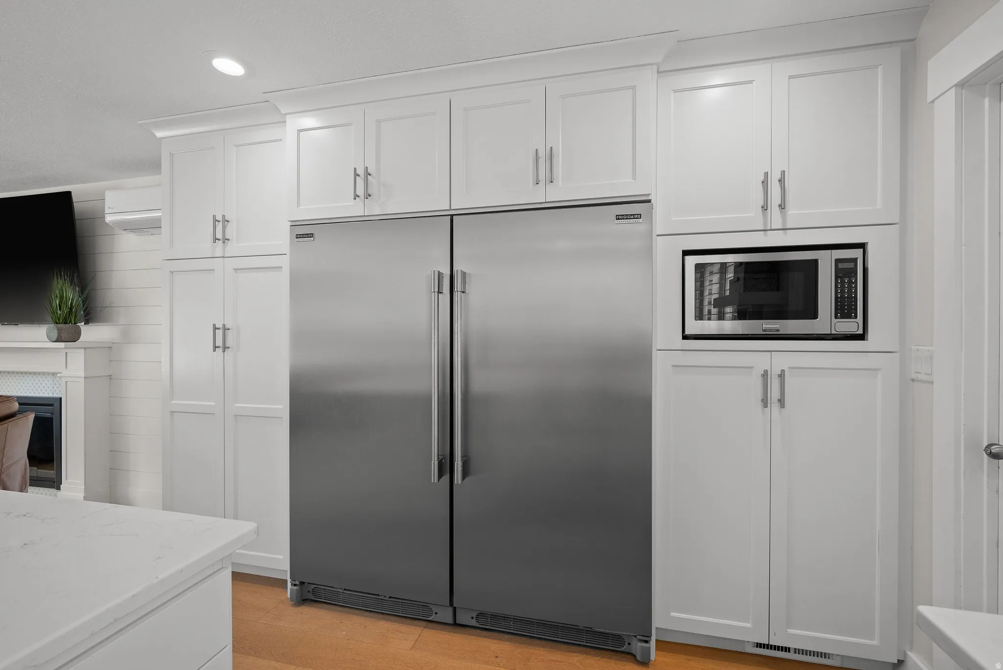 Kitchen with built in appliances, white cabinetry, light wood-style flooring, light stone counters, and a fireplace