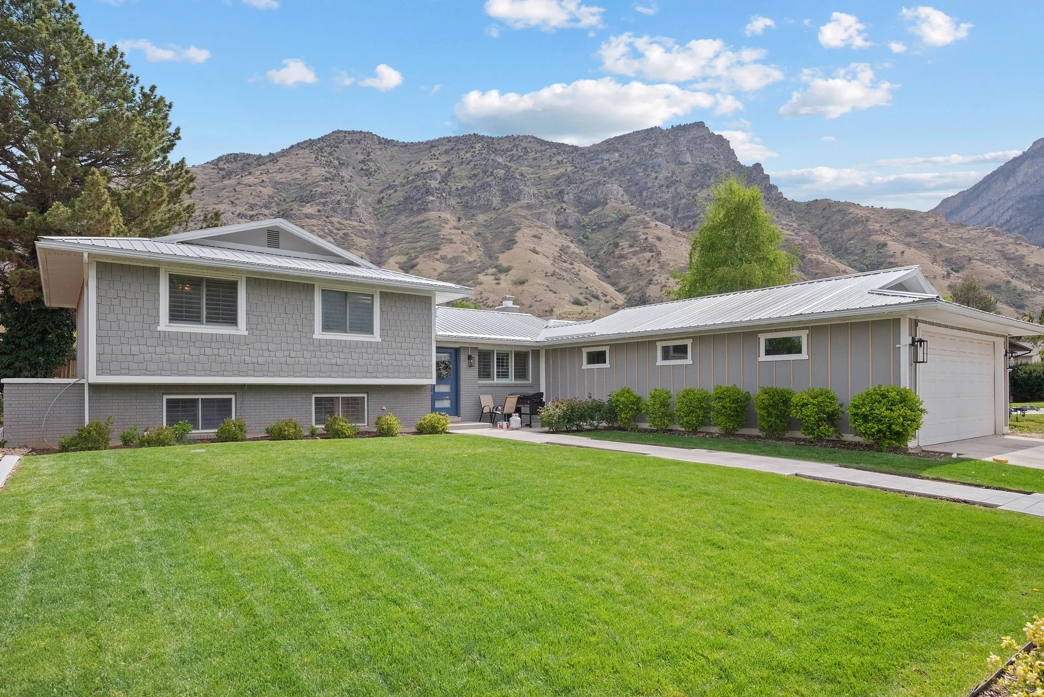 Split level home with a mountain view, a garage, a front lawn, a metal roof, and driveway
