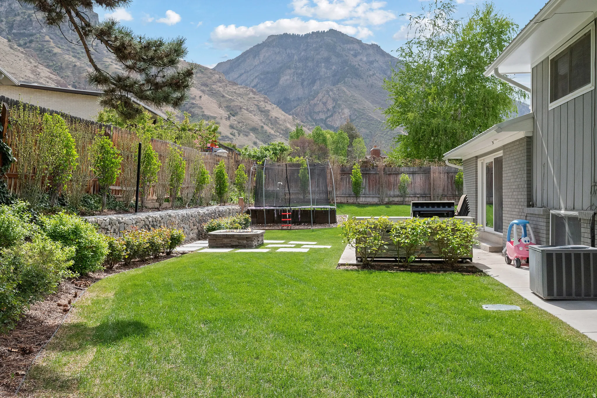 Fenced backyard with a trampoline, a patio area, and a mountain view