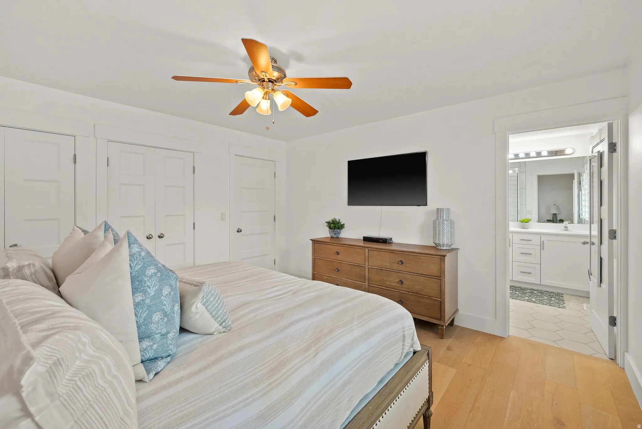 Bedroom with two closets, light wood-type flooring, a ceiling fan, and connected bathroom