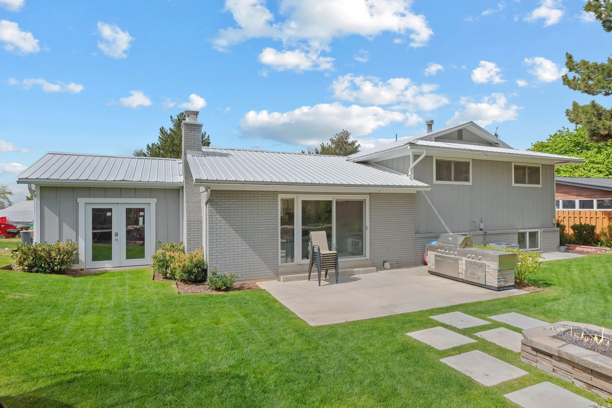 Rear view of house featuring a yard, a metal roof, a chimney, brick siding, and french doors