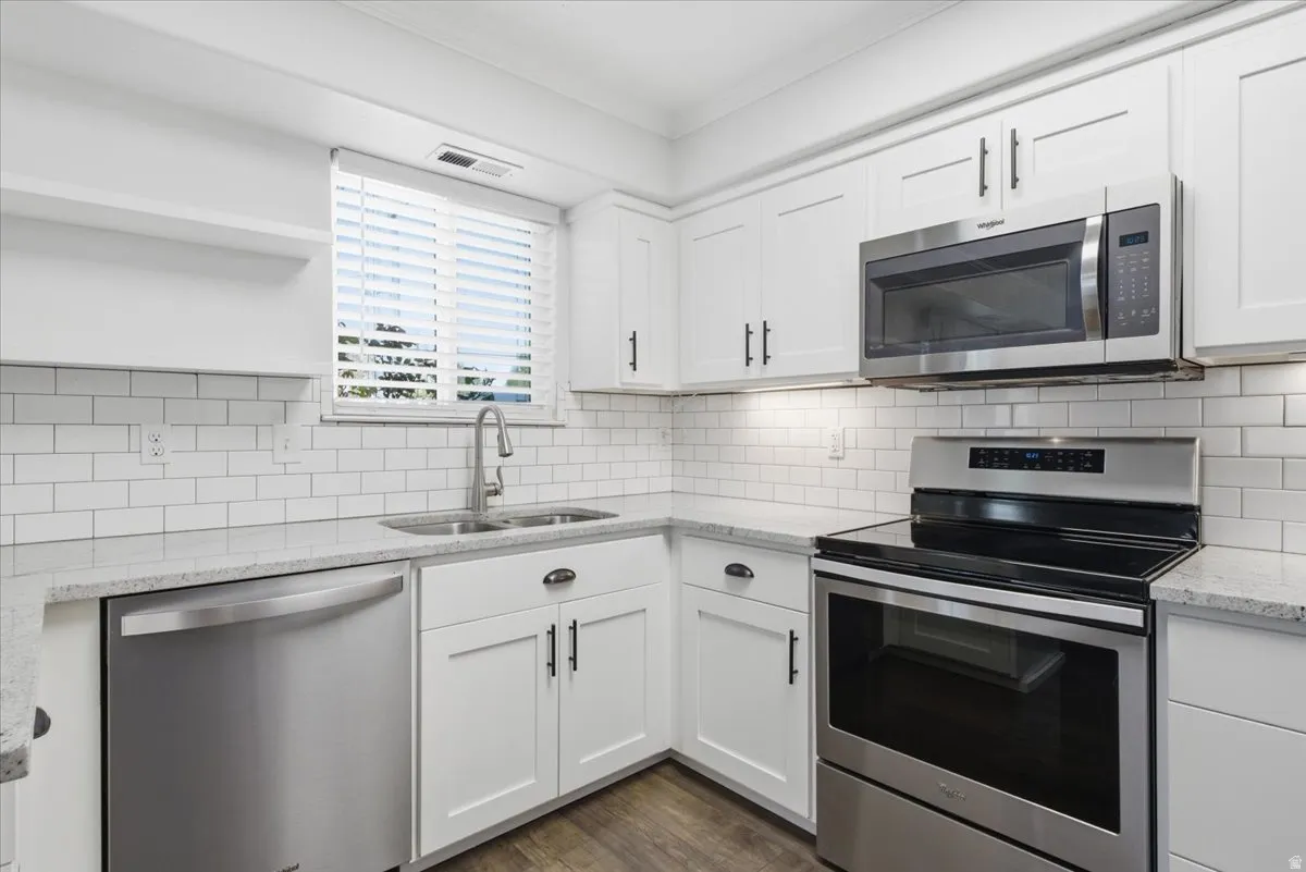 Kitchen with stainless steel appliances, light stone countertops, white cabinets, dark wood-type flooring, and ornamental molding