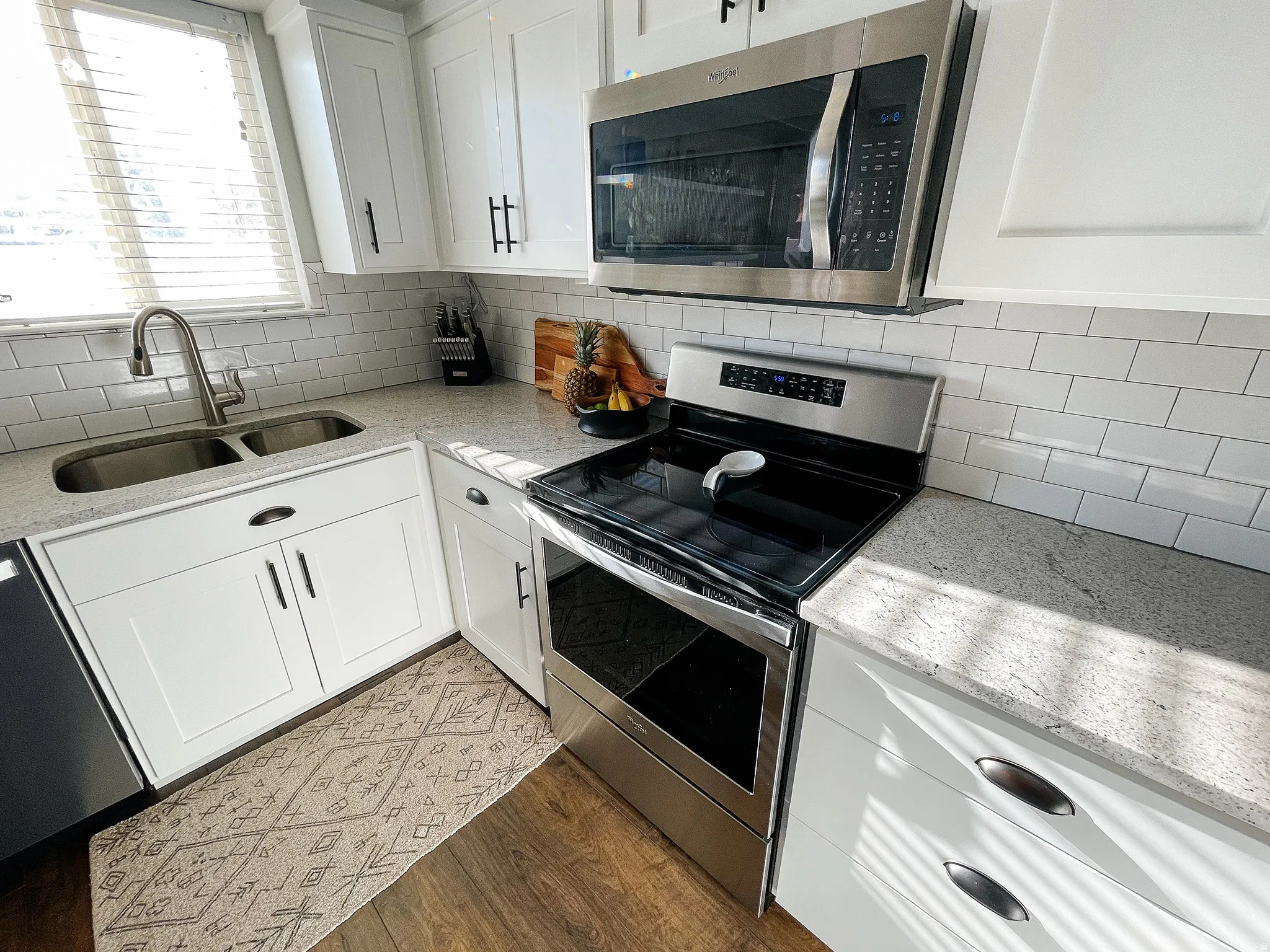 Kitchen with light stone counters, stainless steel appliances, white cabinets, tasteful backsplash, and dark wood-style floors