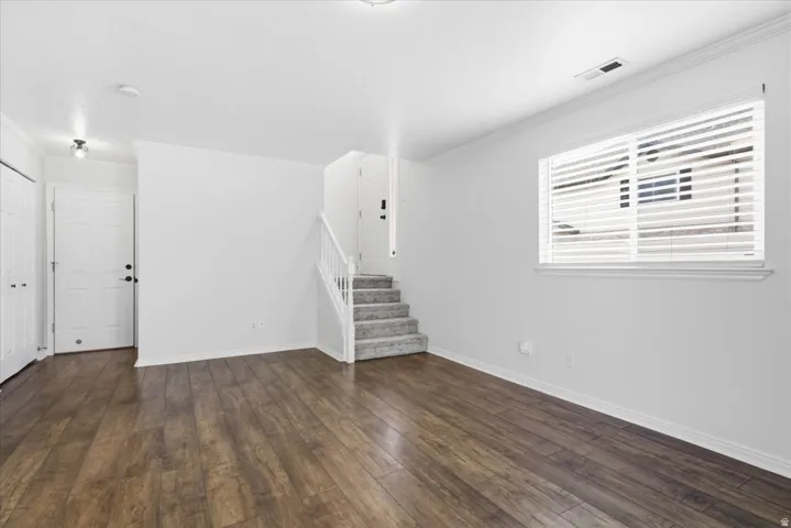Unfurnished living room featuring ornamental molding and dark wood-style flooring